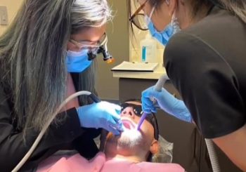 A dental professional uses a scaler and mirror to clean a patient
