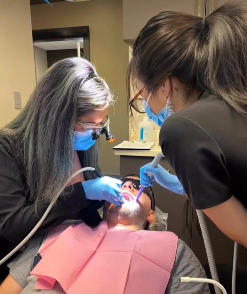 A dental professional uses a scaler and mirror to clean a patient's teeth during a restorative dentistry procedure.