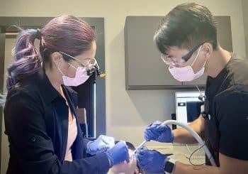 Two dental professionals wearing masks and gloves perform a cosmetic dentistry procedure on a patient in a modern clinic setting.