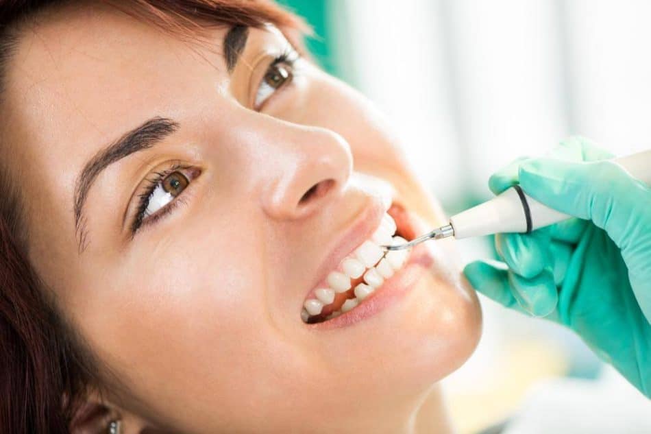 A person receives a dental cleaning with an ultrasonic scaler by a gloved professional, focusing on the teeth and gums to help prevent issues like a knocked-out tooth.