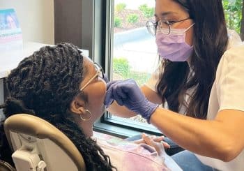 A dentist wearing a mask and gloves examines a patient
