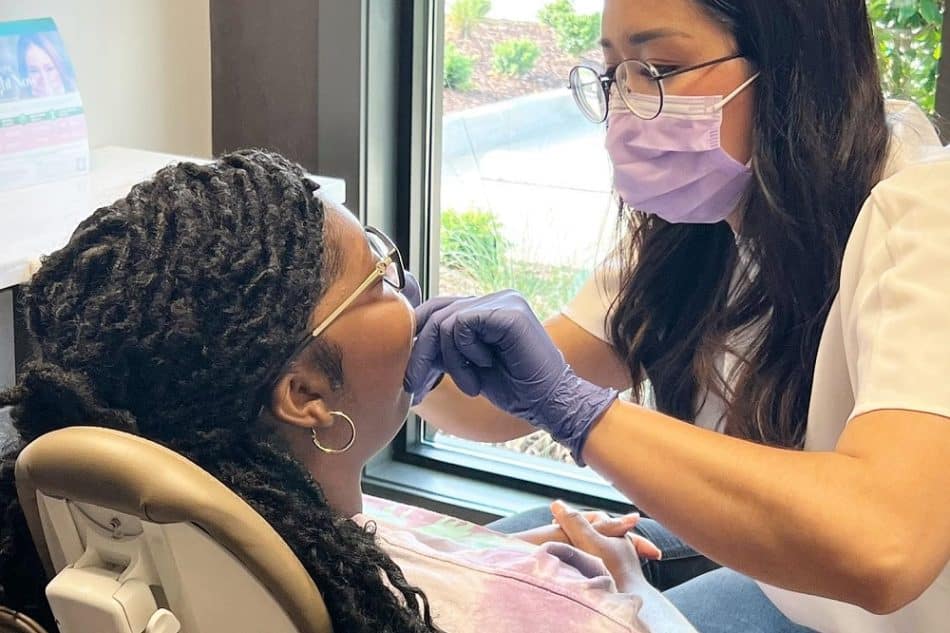 A dentist wearing a mask and gloves examines a patient