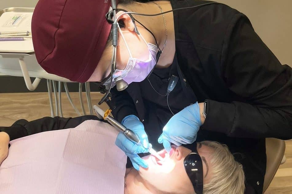 A dentist wearing gloves and a face mask examines a patient