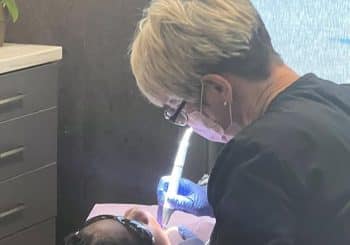 A dental professional wearing gloves and a mask examines a patient