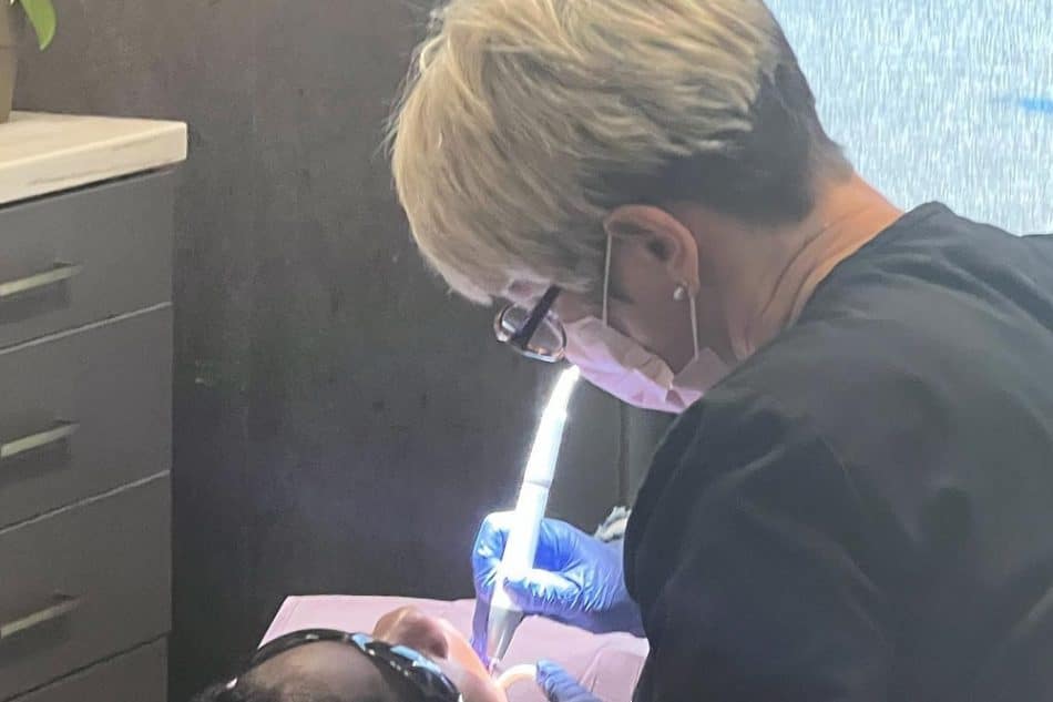 A dental professional wearing gloves and a mask examines a patient